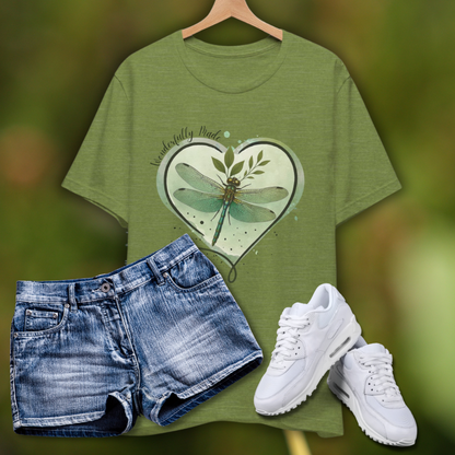 Olive green “Wonderfully Made” dragonfly T-shirt displayed with denim shorts and white sneakers on a soft green nature-inspired background; features a heart-shaped watercolor design with a botanical dragonfly and Christian message.